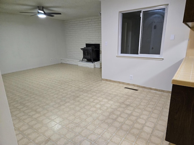 unfurnished living room with visible vents, baseboards, light floors, a wood stove, and a ceiling fan