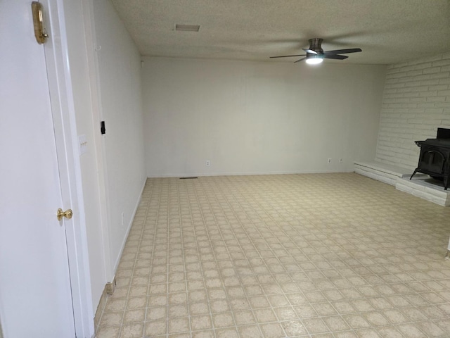 unfurnished living room with a textured ceiling, a wood stove, light floors, and ceiling fan