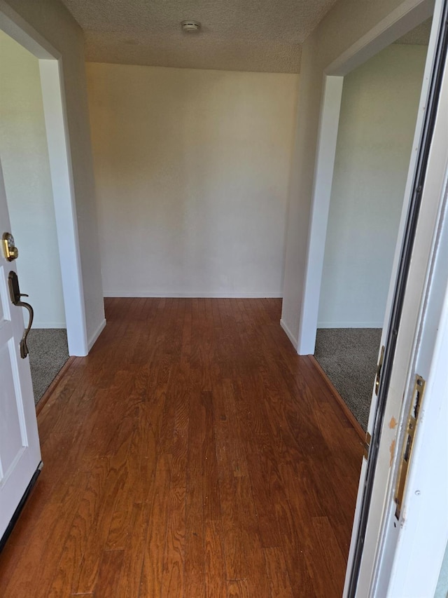 hall featuring baseboards, a textured ceiling, and wood finished floors