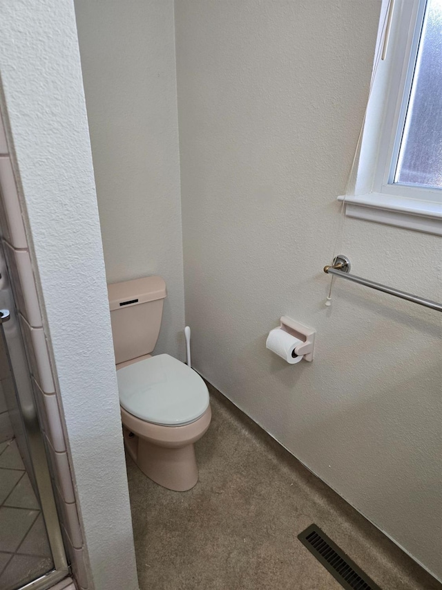 bathroom featuring a shower with door, visible vents, toilet, and a textured wall