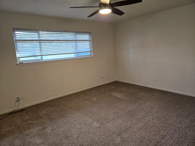 empty room with dark carpet, a ceiling fan, and baseboards