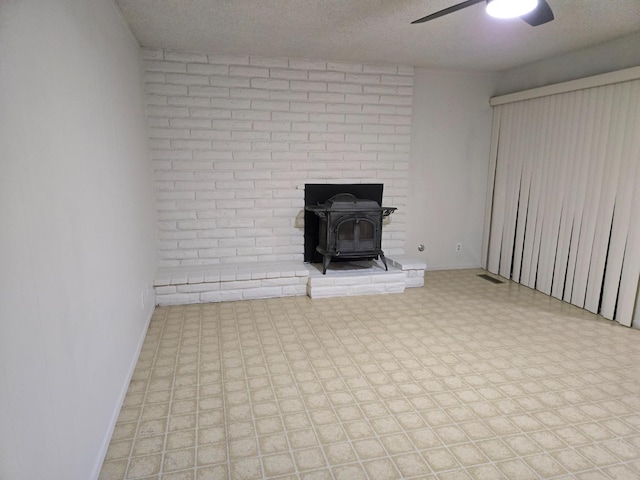 unfurnished living room with tile patterned floors, baseboards, a textured ceiling, and a wood stove