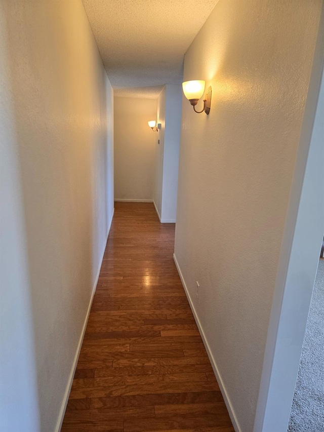 hall featuring dark wood-type flooring, a textured wall, baseboards, and a textured ceiling