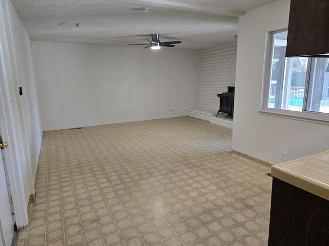 unfurnished living room with a ceiling fan, a wood stove, light floors, and a textured ceiling