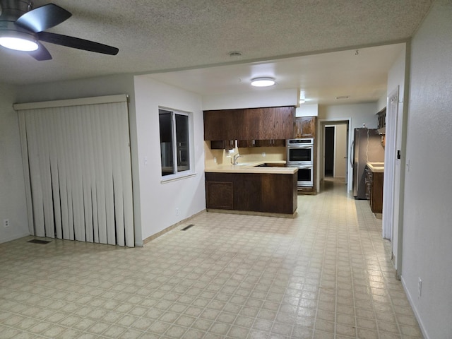 kitchen with light floors, a peninsula, stainless steel appliances, dark brown cabinetry, and light countertops