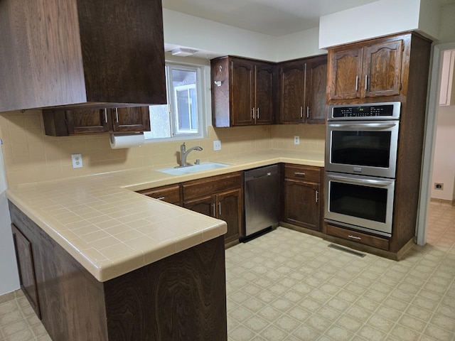 kitchen featuring tasteful backsplash, dark brown cabinets, light floors, appliances with stainless steel finishes, and a sink