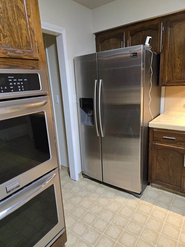 kitchen with light floors, tile counters, dark brown cabinetry, appliances with stainless steel finishes, and tasteful backsplash