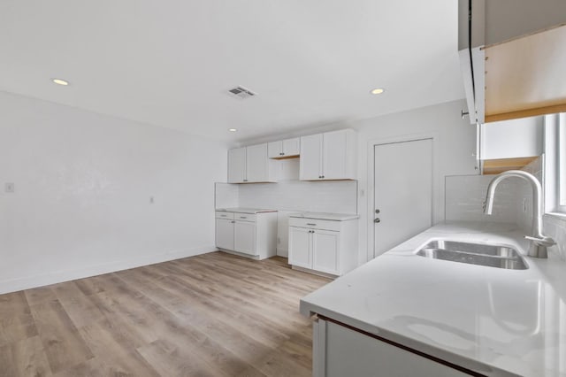 kitchen with visible vents, backsplash, white cabinetry, and a sink