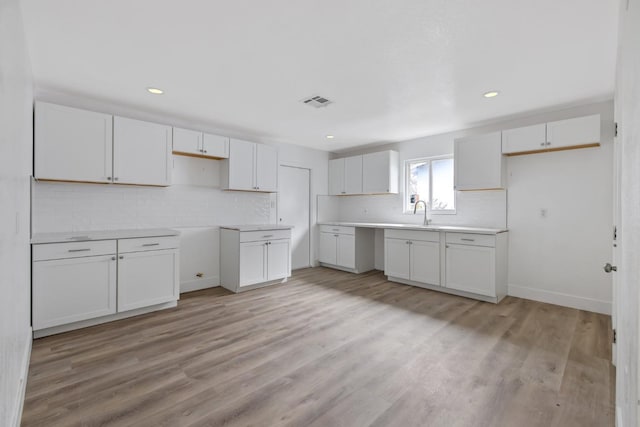 kitchen with decorative backsplash, white cabinetry, and light wood-type flooring