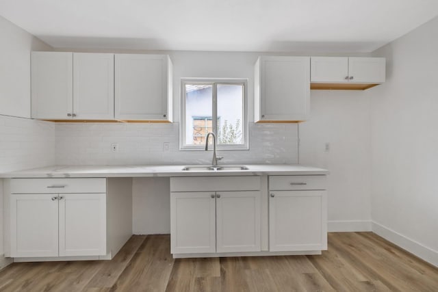 kitchen with white cabinetry, light wood-type flooring, backsplash, and a sink