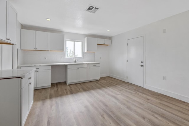 kitchen with visible vents, a sink, backsplash, light wood-style floors, and baseboards