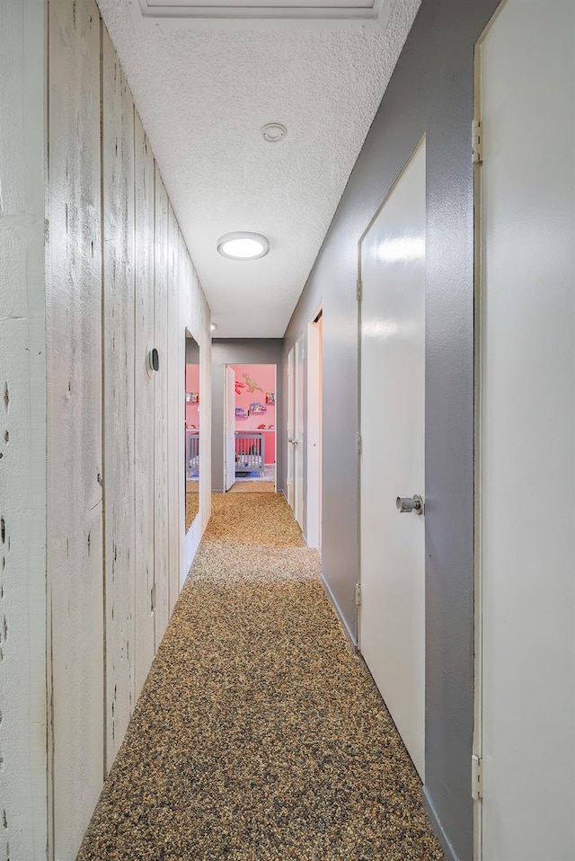 corridor featuring carpet floors, a textured ceiling, and wooden walls