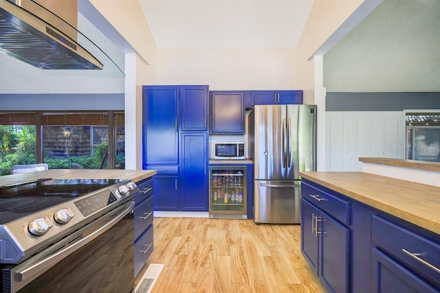 kitchen with ventilation hood, wooden counters, blue cabinetry, wine cooler, and appliances with stainless steel finishes