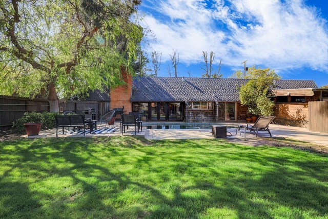 rear view of house with a fenced in pool, fence, a lawn, a chimney, and a patio