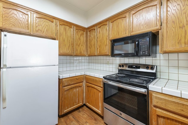 8153 N Cedar Ave Unit 106, Fresno, CA 93720 - kitchen with freestanding refrigerator, stainless steel range with electric stovetop, black microwave, tile counters, and light wood-style flooring