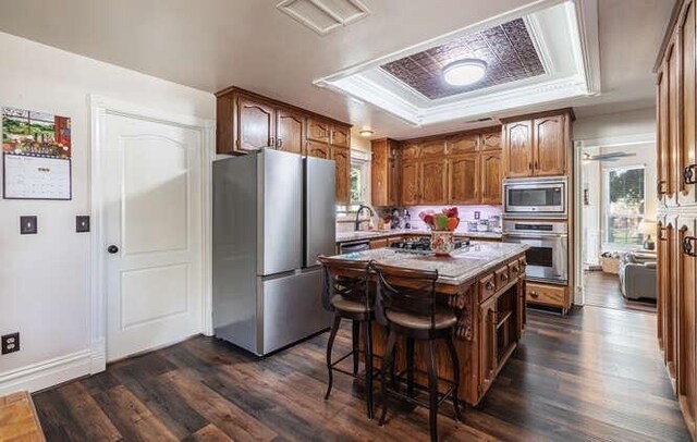 26189 Valerie Ave, Madera, CA 93638 - kitchen with stainless steel appliances, a tray ceiling, dark wood finished floors, a kitchen island, and a breakfast bar