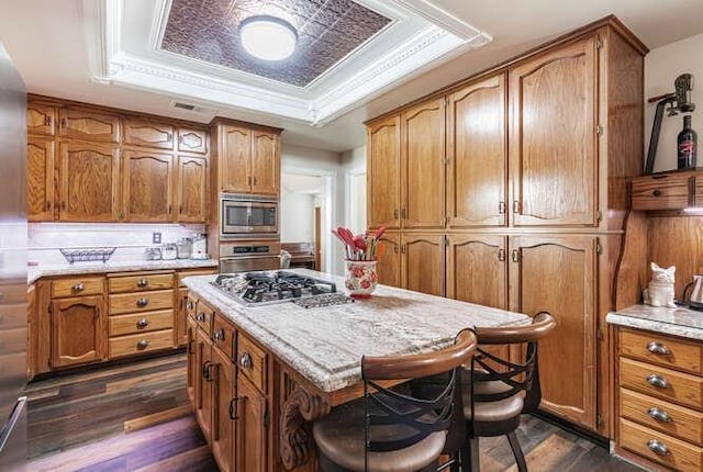 26189 Valerie Ave, Madera, CA 93638 - kitchen with a raised ceiling, stainless steel appliances, dark wood-type flooring, brown cabinetry, and a kitchen island