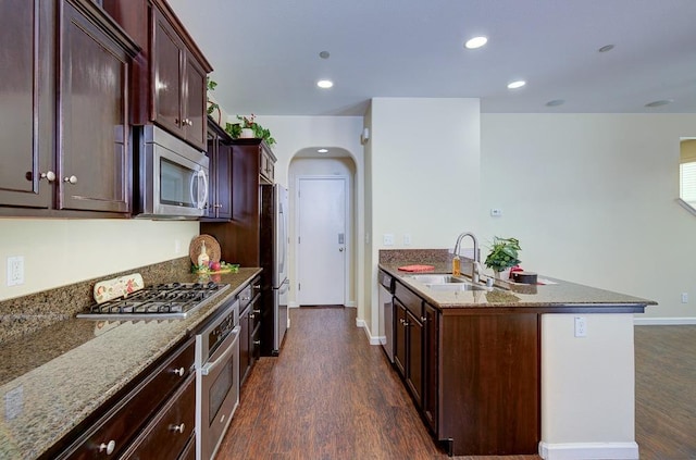 kitchen with arched walkways, stone counters, stainless steel appliances, and a sink