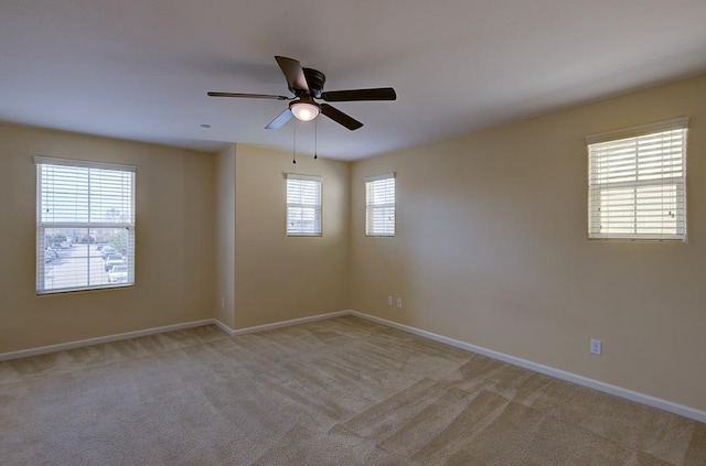 empty room featuring a ceiling fan, light colored carpet, and baseboards