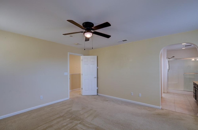 unfurnished bedroom with baseboards, visible vents, arched walkways, ceiling fan, and light carpet