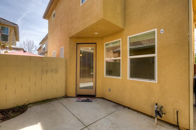 view of exterior entry featuring a patio, fence, and stucco siding