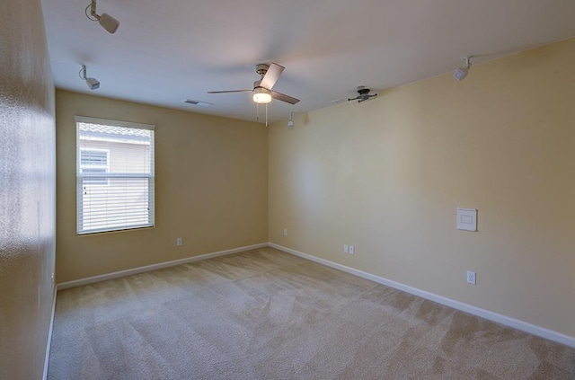 empty room featuring a ceiling fan, light colored carpet, visible vents, and baseboards