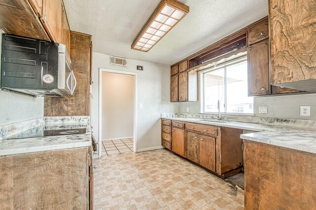 kitchen featuring visible vents, a sink, a textured ceiling, brown cabinetry, and light countertops