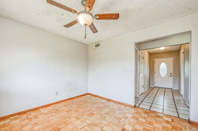 empty room with baseboards, a ceiling fan, visible vents, and a textured ceiling