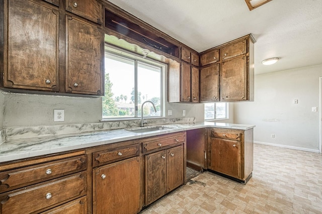 kitchen featuring light countertops, a peninsula, baseboards, and a sink