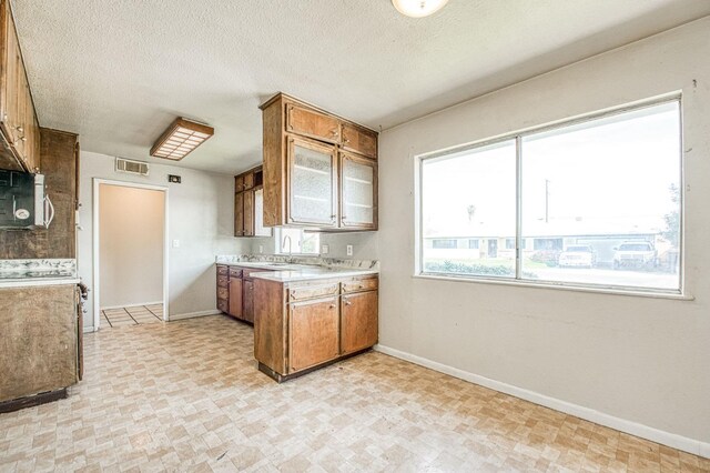 kitchen featuring visible vents, gas range, light countertops, a peninsula, and brown cabinetry