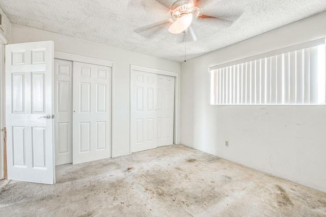 unfurnished bedroom with a textured ceiling, multiple closets, and a ceiling fan