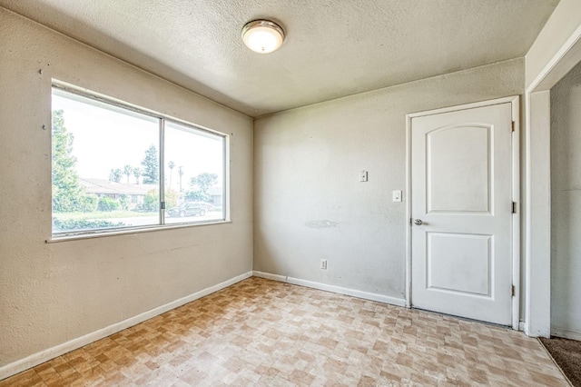 spare room featuring a textured wall, baseboards, and a textured ceiling