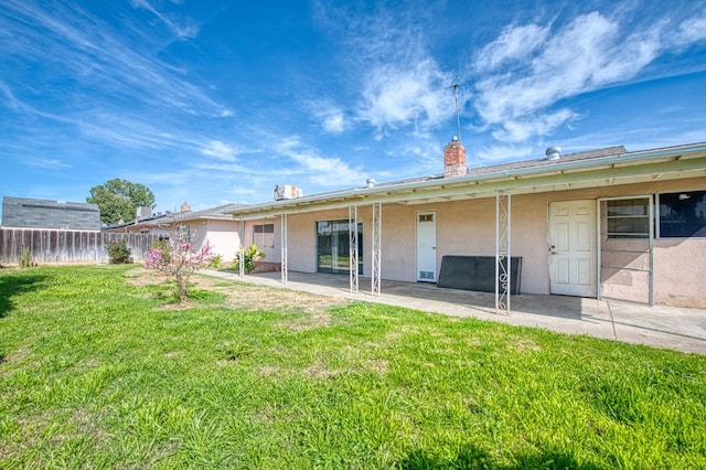 rear view of house with fence, a yard, a chimney, stucco siding, and a patio area