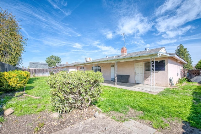 rear view of property featuring stucco siding, a lawn, a fenced backyard, a chimney, and a patio area