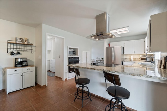 kitchen with light stone countertops, a peninsula, a sink, stainless steel appliances, and island range hood