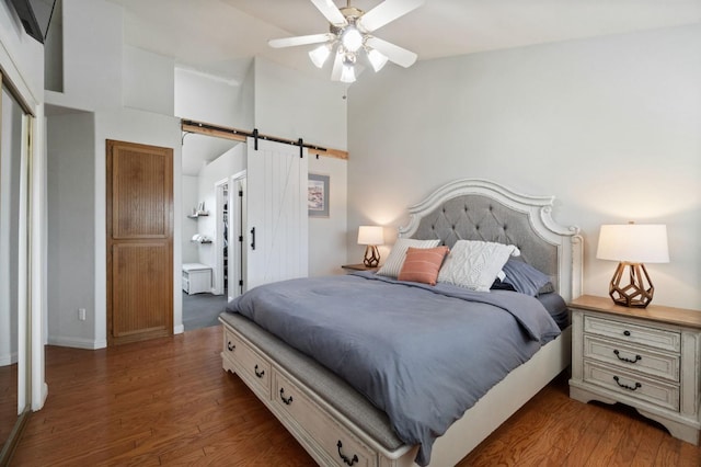 bedroom with connected bathroom, a barn door, high vaulted ceiling, and wood finished floors