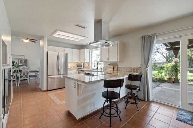 kitchen with visible vents, freestanding refrigerator, a peninsula, light tile patterned flooring, and light stone countertops