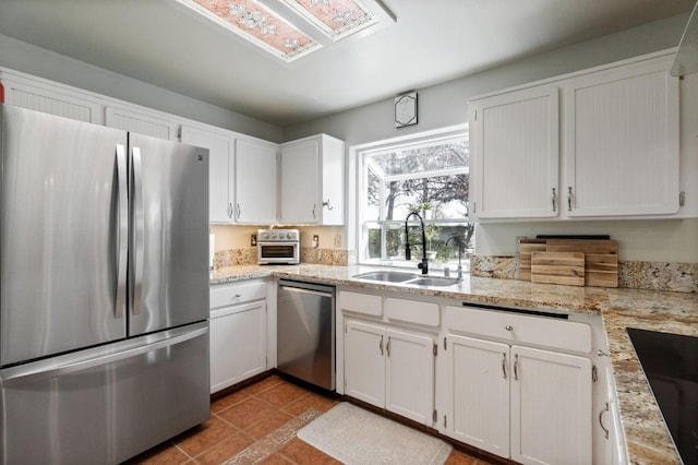 kitchen with tile patterned flooring, light stone countertops, stainless steel appliances, white cabinetry, and a sink