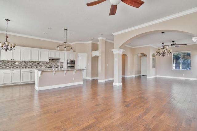 unfurnished living room with light wood-style flooring, ceiling fan with notable chandelier, baseboards, and ornamental molding