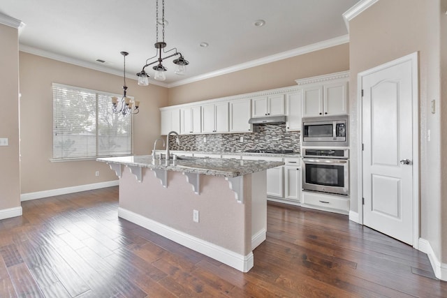 kitchen with ornamental molding, a sink, under cabinet range hood, a kitchen breakfast bar, and appliances with stainless steel finishes