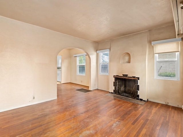 unfurnished living room with baseboards, arched walkways, a fireplace, and hardwood / wood-style flooring