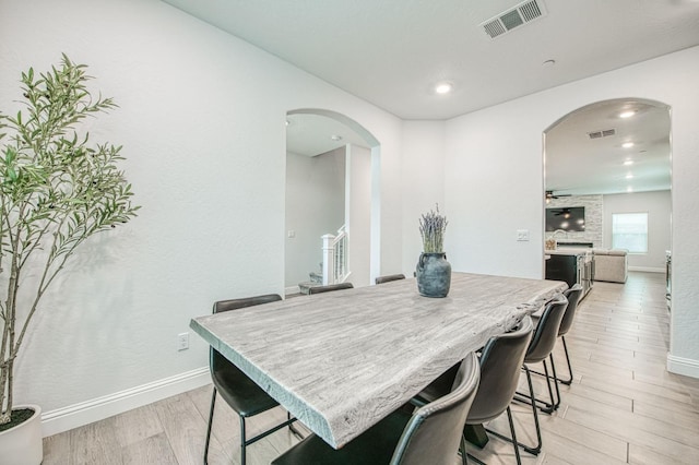 dining room featuring light wood-style flooring, arched walkways, visible vents, and baseboards