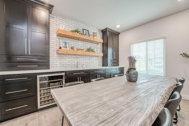 kitchen with backsplash, beverage cooler, light countertops, light wood-type flooring, and a kitchen breakfast bar