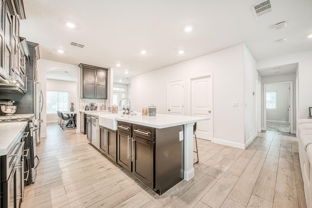 kitchen with visible vents, a center island with sink, light wood-style flooring, arched walkways, and a sink