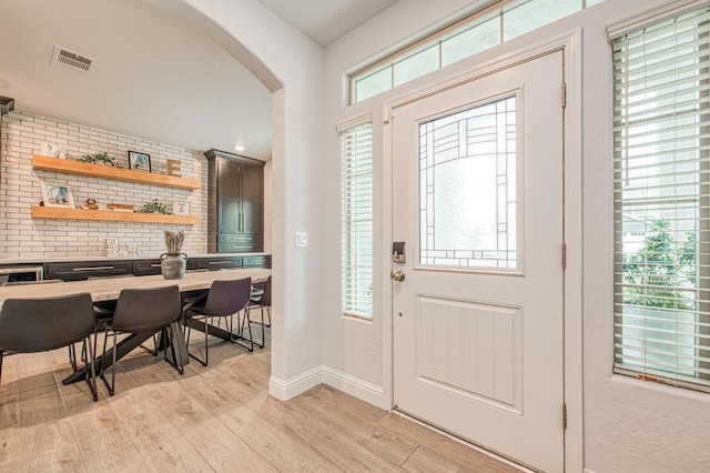 entryway featuring visible vents, arched walkways, light wood finished floors, and baseboards