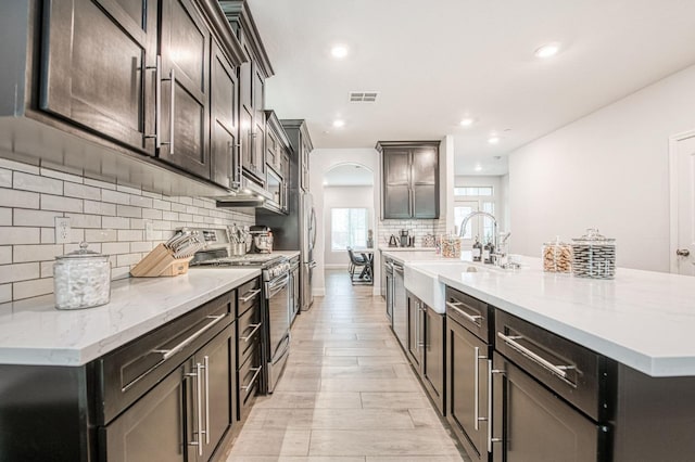 kitchen featuring tasteful backsplash, light wood-style floors, arched walkways, stainless steel appliances, and a sink