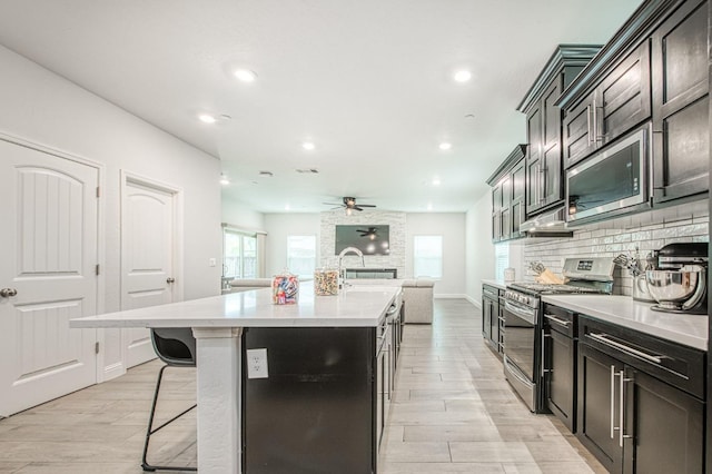 kitchen featuring backsplash, a kitchen bar, light countertops, an island with sink, and appliances with stainless steel finishes