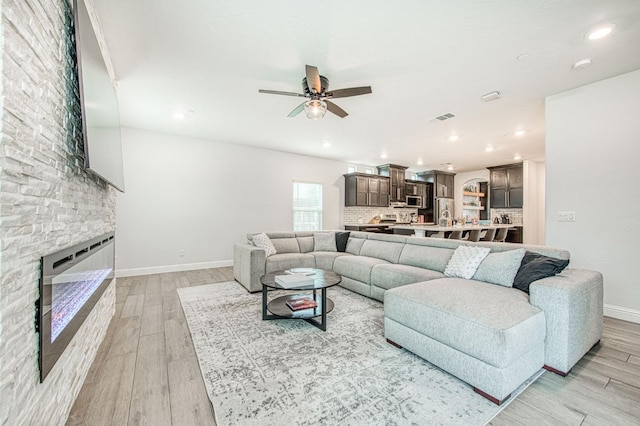 living room with heating unit, baseboards, visible vents, light wood-style flooring, and a large fireplace