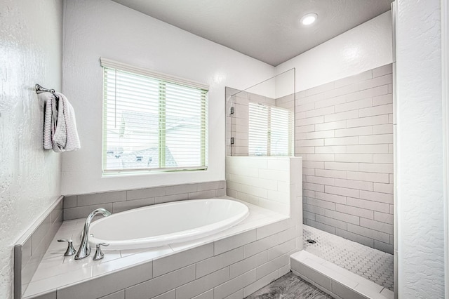 full bath featuring a textured wall, a garden tub, and a walk in shower