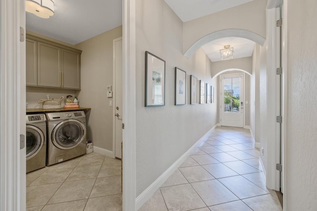 laundry room featuring washer and clothes dryer, cabinet space, arched walkways, light tile patterned floors, and baseboards